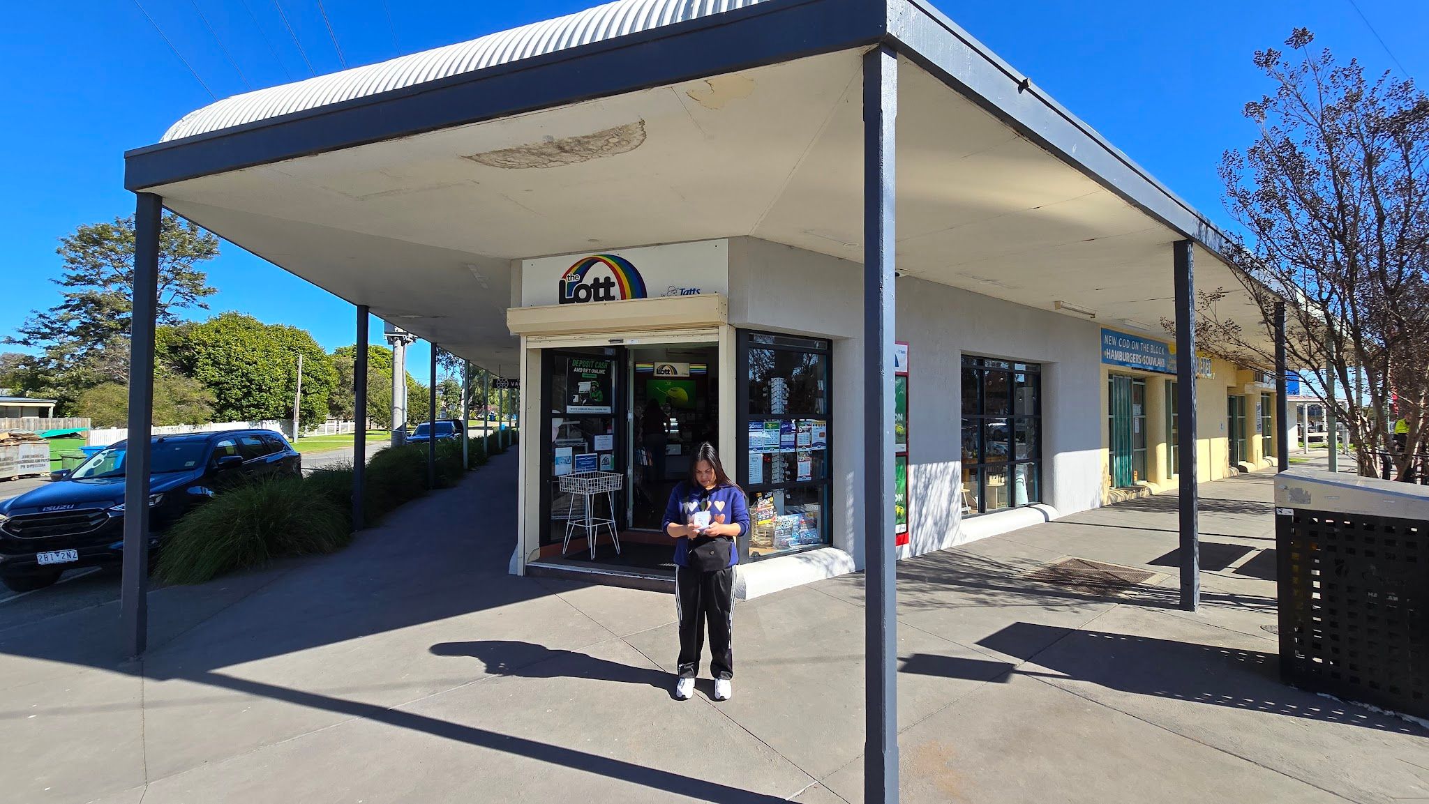 Tooradin News storefront with lottery signage and staff member under flat awning, blue sky